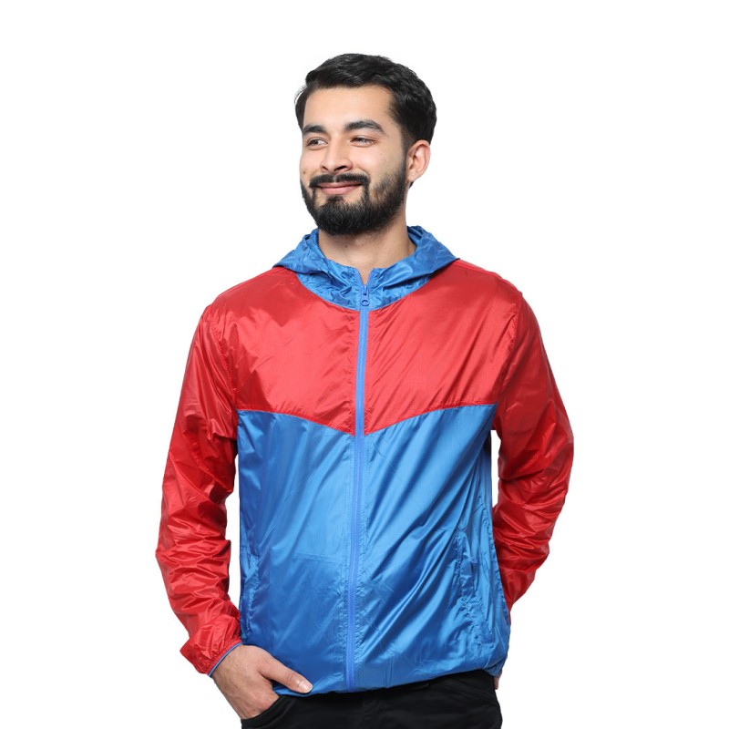 A smiling male model wearing the lightweight SkyShield Windcheater Jacket, featuring a bold red and bright blue color-block design, a full front zipper and an adjustable hood